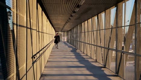 Person-in-trench-coat-cross-metal-cage-bridge-over-traffic-talking-on-phone