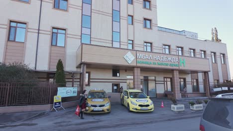 Personas-Y-Automóviles-Frente-A-La-Entrada-Principal-Del-Hospital-De-Salud-Para-Mujeres-De-Nadezhda-En-Un-Ventoso-Día-De-Invierno