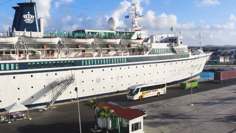 Ein-Kleines-Kreuzfahrtschiff-Liegt-Im-Hafen,-Während-In-Der-Nähe-Ein-Bus-Wartet,-Der-Bereit-Ist,-Passagiere-Zu-Ihrem-Nächsten-Ausflug-Vom-Geschäftigen-Hafen-Aus-Einzuschiffen