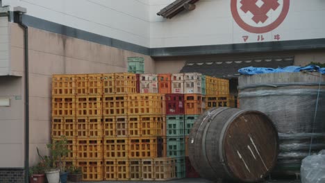 Colorful-beverage-crates-stacked-in-Oki-Town,-Japan-with-traditional-architecture,-under-a-cloudy-sky