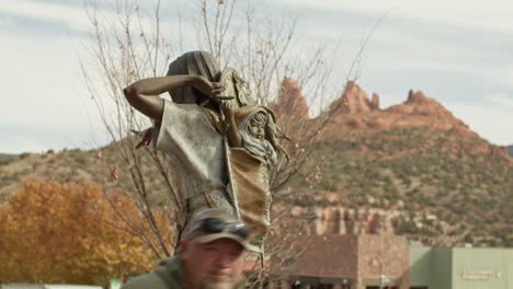 Indianische-Frau-Mit-Baby-In-Papoose-Skulptur-In-Der-Innenstadt-Von-Sedona,-Arizona,-Mit-Menschen,-Die-Vorbeigehen