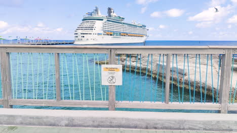 Amidst-the-grandeur-of-docked-cruise-ship,-whimsical-caution-sign-on-the-bridge-adds-touch-of-humor-to-the-bustling-waterfront-scene-|-funny-caution-sign-on-island-with-cruise-ship-docked