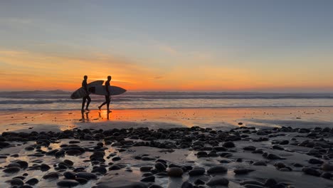 Siluetas-De-Surfistas-Caminando-Por-La-Playa-Durante-Una-Hermosa-Puesta-De-Sol