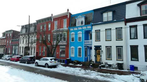 Fila-De-Casas-Coloridas-Con-Nieve-En-La-Acera-Y-Autos-Estacionados