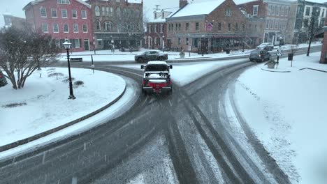 Camioneta-Con-Quitanieves-Y-Esparcimiento-De-Sal-Conduciendo-Por-La-Pequeña-Plaza-Cubierta-De-Nieve-Y-Adornos-Navideños