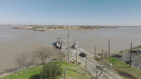 Una-Toma-Aérea-Del-Atraque-Del-Ferry-De-Lynchburg,-Con-Automóviles-Descargando-En-El-Sitio-Del-Campo-De-Batalla-De-San-Jacinto-A-Lo-Largo-Del-Canal-De-Navegación-De-Houston-En-La-Porte,-Texas.