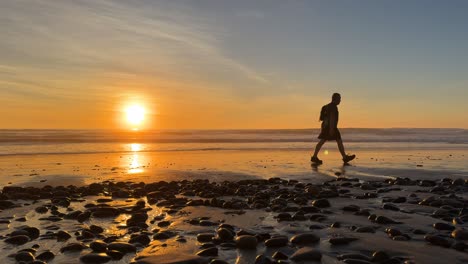 Silhouette-Eines-Wanderers,-Der-Während-Eines-Wunderschönen-Sonnenuntergangs-Am-Strand-Spaziert