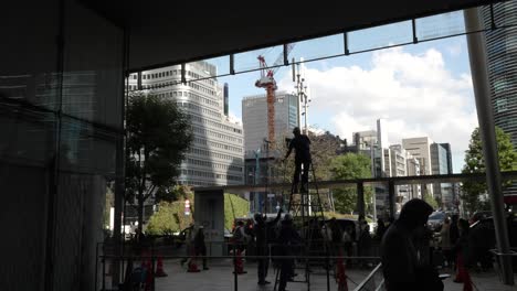 Vista-De-La-Silueta-De-Los-Trabajadores-De-Mantenimiento-De-La-Estación-De-Tokio-Limpiando-Ventanas-En-El-Lado-De-Entrada-De-Yaesu-Con-Viajeros-Caminando