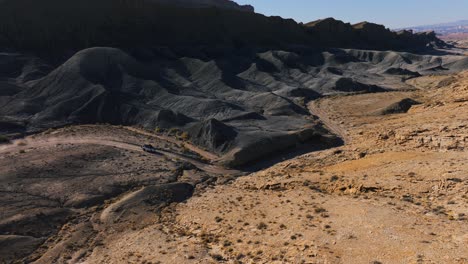 SUV-drives-through-rugged-desert-landscape-near-Factory-Butte-with-black-rock-formations