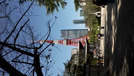 Visitantes-Caminando-Fuera-Del-Patio-Al-Lado-Del-Templo-Zojoji-Con-Vistas-A-La-Torre-De-Tokio-Y-Las-Colinas-Azabudai-Contra-El-Cielo-Azul