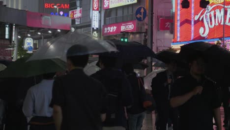 Viele-Einheimische-Laufen-Nachts-Durch-Ein-Regnerisches-Tokio-Mit-Vielen-Lichtern-Im-Hintergrund