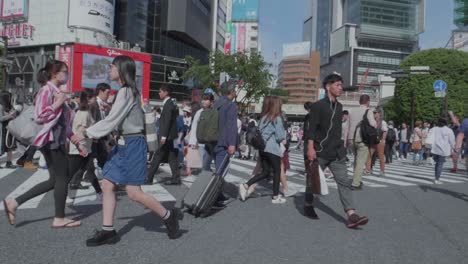 Thousands-of-People-walking-over-the-world-famous-Shibuya-Crossing,-which-is-the-busiest-intersection-in-the-world,-on-a-beautiful-sunny-day-in-slow-motion