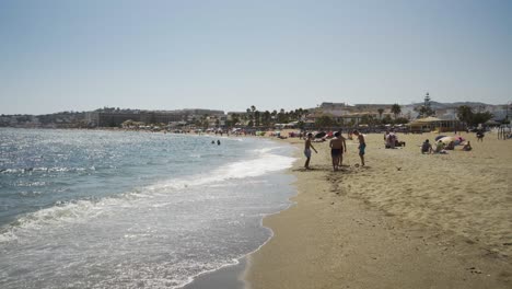 Ein-Wunderschöner-Blick-Entlang-Des-Strandes-Von-Cala-De-Mijas,-Während-Familien-Die-Sonne-Genießen-Und-Eine-Gruppe-Jungs-Am-Strand-Wache-Spielt