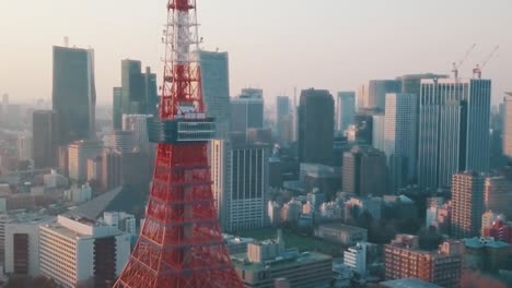 Drone-Aéreo-Sobre-La-Ciudad-De-Tokio-Panorámica-Alrededor-De-La-Icónica-Torre-Roja-De-Tokio-Rodeada-De-Altos-Rascacielos-Durante-Una-Impresionante-Puesta-De-Sol-Con-Cielos-Azules-Y-Naranjas