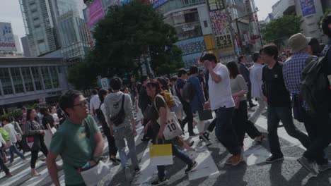 Thousands-of-People-walking-over-the-world-famous-Shibuya-Crossing,-which-is-the-busiest-intersection-in-the-world,-on-a-beautiful-sunny-day-in-slow-motion