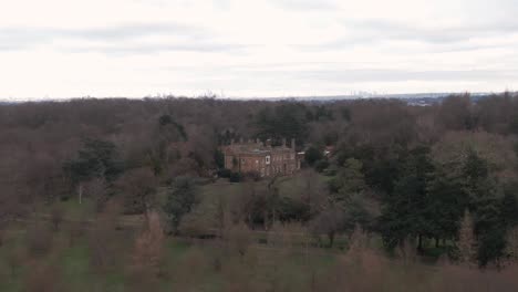 Aerial-drone-shot-of-Addington-Palace-in-Croydon,-London,-United-Kingdom-on-a-cloudy-day-and-with-London-Downtown-Cityscape-in-the-background