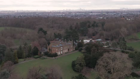 Aerial-drone-shot-of-Addington-Palace-in-Croydon,-London,-United-Kingdom-on-a-cloudy-day-and-with-London-Downtown-Cityscape-in-the-background