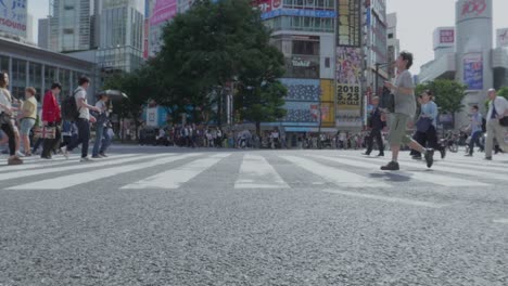 Thousands-of-People-walking-over-the-world-famous-Shibuya-Crossing,-which-is-the-busiest-intersection-in-the-world,-on-a-beautiful-sunny-day-in-slow-motion