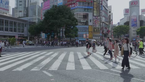 Thousands-of-People-walking-over-the-world-famous-Shibuya-Crossing,-which-is-the-busiest-intersection-in-the-world,-on-a-beautiful-sunny-day-in-slow-motion