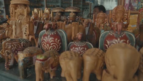 Panning-From-A-Large-Brown-Cow-Walking-Down-The-Streets-Of-India-To-A-Market-Stall-Selling-Wooden-Ornaments