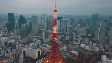 Drone-aerial-above-Tokyo-City-panning-towards-the-Tokyo-Tower-surrounded-by-tall-skyscrapers-at-dusk-with-moody-dark-overcast-clouds-and-smog-polluted-skies