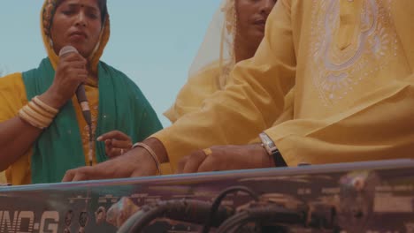 Un-Hombre-Tocando-El-Piano-En-Una-Boda-Tradicional-India-Con-Una-Mujer-India-Vestida-Con-Un-Sari-Parada-Al-Fondo-Con-Un-Micrófono