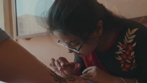 An-Indian-woman-creating-a-traditional-henna-tattoo-on-the-hand-of-a-female-tourist-in-Jaipur,-India