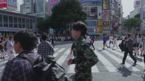 Thousands-of-People-walking-over-the-world-famous-Shibuya-Crossing,-which-is-the-busiest-intersection-in-the-world,-on-a-beautiful-sunny-day-in-slow-motion