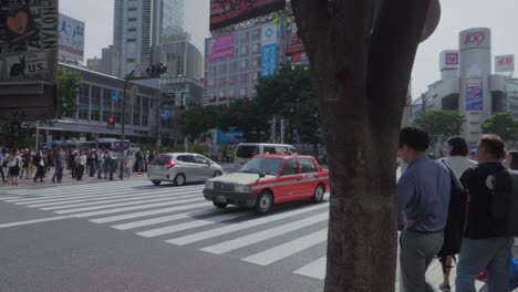 Many-cars-driving-over-the-huge-Shibuya-Crossing-in-Tokyo,-Japan-on-a-sunny-day