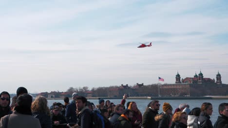 Helicóptero-De-La-Guardia-Costera-Estadounidense-Sobrevolando-La-Isla-Ellis-Con-Gente-En-Un-Ferry-En-Primer-Plano-A-Cámara-Lenta