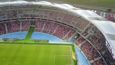 aerial-shot-of-a-professional-soccer-field-where-a-match-is-taking-place-between-a-team-in-white-uniforms-and-another-in-red-uniforms-during-day-time