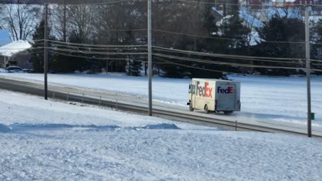 FedEx-delivery-truck-driving-on-snow-covered-road-in-rural-USA-in-winter