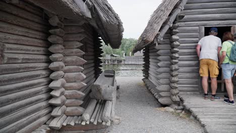 Visitors-exploring-traditional-log-structures-at-an-Ice-Age-museum,-Friedrichshafen,-canoe-in-foreground