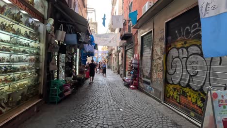 POV-Aufnahme-Eines-Spaziergangs-Durch-Eine-Schmale-Straße-Mit-Graphit-Im-Stadtzentrum-Mit-Geschäften-Mit-Souvenirs-Aus-Neapel-In-Italien