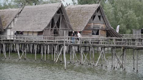 Reetdachhäuser-Auf-Stelzen-über-Dem-Wasser,-Besucher-Auf-Dem-Gehweg,-Historische-Rekonstruktion,-Eiszeitmuseum-Friedrichshafen