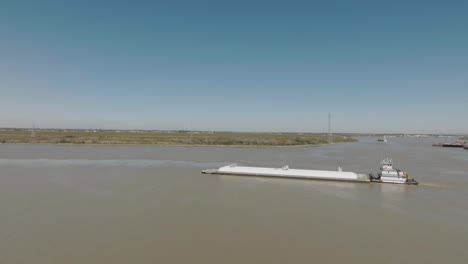 An-aerial-view-of-a-tugboat-pushing-a-barge-up-the-Houston-Ship-Channel-under-the-clear-blue-skies-of-Houston,-Texas