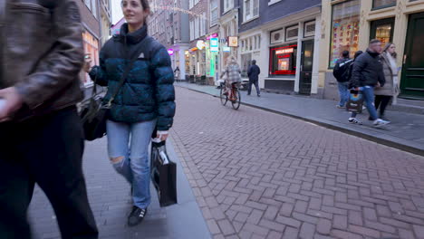 Amsterdamer-Durchgangsstraße,-Verschiedene-Fußgänger,-Frau,-Die-Einen-Kinderwagen-Schiebt,-Mann,-Der-Fahrrad-Inspiziert,-Einkaufstaschen,-Winterkleidung,-Enge-Straße,-Niederländische-Gebäude,-Hängende-Girlanden,-Kühle-Atmosphäre