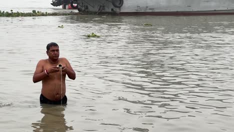 Profile-view-of-a-man-talking-the-holy-dip-and-praying-in-foggy-winter-morning-during-Sankranti-with-jetty-in-the-background-in-Babughat,-Kolkata