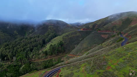 Beautiful-aerial-shot-of-a-race-on-the-edge-of-the-mountains-surrounded-by-nature,-trees-and-low-clouds-from-the-Golden-Gate-viewpoint