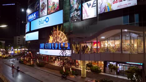 Slow-moving-traffic-cruising-on-a-street-in-front-of-popular,-cinema-in-the-middle-of-Bangkok,-Thailand