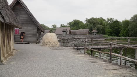 Woman-exploring-outdoor-Ice-Age-museum-in-Friedrichshafen,-traditional-wooden-structures-and-walkways,-overcast-day