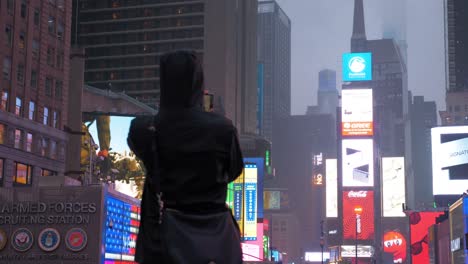 Silueta-Tomando-Fotografías-Con-Un-Teléfono-Inteligente-Por-La-Noche-En-Time-Square,-Con-Todas-Las-Pantallas-De-Los-Edificios,-La-Ciudad-De-Nueva-York