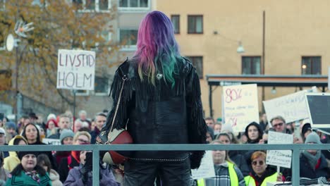 Activist-Linnea-Claeson-at-women's-rights-rally,-facing-a-crowd-with-protest-signs,-urban-setting