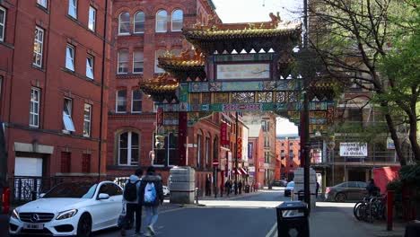 Fußgänger,-Die-Tagsüber-Unter-Dem-Reich-Verzierten-Chinatown-Tor-In-Manchester-Laufen,-Klarer-Himmel