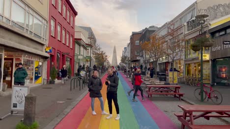 Colorful-street-in-Reykjavik-with-pedestrians,-vibrant-buildings,-and-the-iconic-Hallgrimskirkja-in-the-background