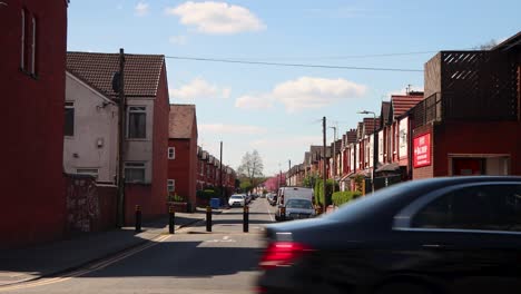 Reihe-Roter-Backsteinhäuser-Unter-Blauem-Himmel-In-Manchester,-Fußgänger-überqueren-Die-Straße,-Geparkte-Autos,-Sonniger-Tag