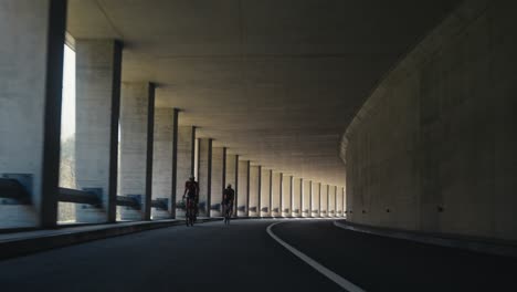 Zwei-Rennradfahrer-Fahren-Mit-Ihren-Fahrrädern-In-Einem-Tunnel-Hintereinander-In-Voller-Montur