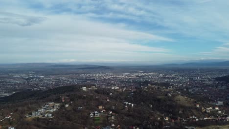 Aerial-shot-of-a-city-surrounded-by-mountains-under-the-blue-sky-and-its-clouds