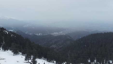 incredible-aerial-drone-shot-of-mountains-full-of-pine-trees-and-snow,-during-a-snowfall-in-winter