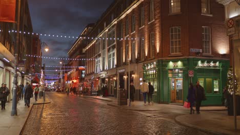 Escena-Crepuscular-En-Una-Bulliciosa-Calle-De-Dublín-Adornada-Con-Luces-Festivas,-Gente-Caminando